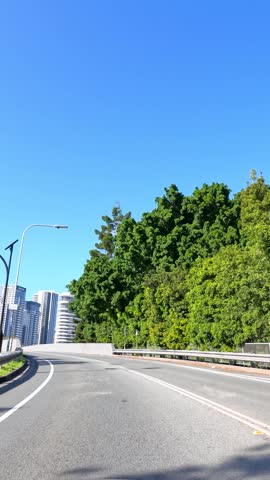 Forward-facing vehicle camera captures urban road driving toward modern skyscrapers under clear blue sky.
