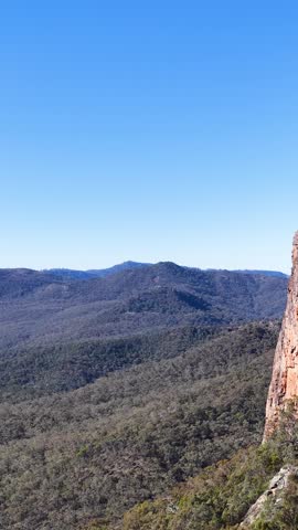 A wedge-tailed eagle glides past the iconic Breadknife rock formation under a clear sky.