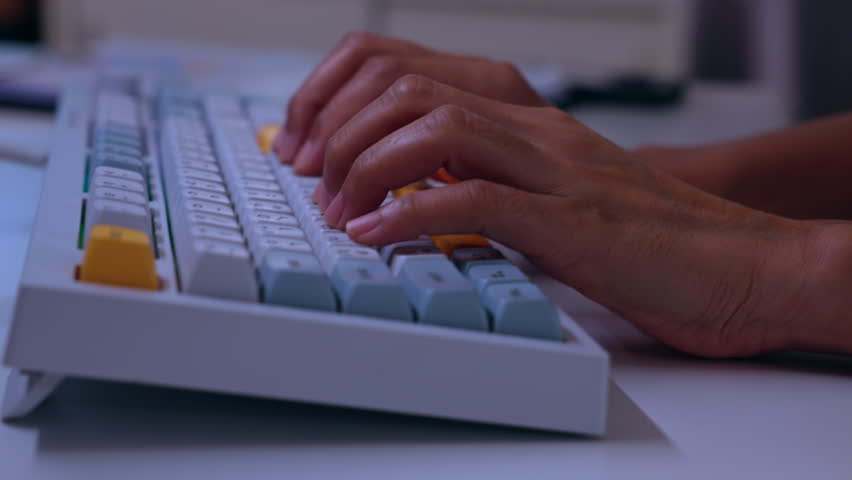 Hands typing on colorful mechanical keyboard at office desk closeup, computer key input for work, study, writing, data entry, communication, technology workstation