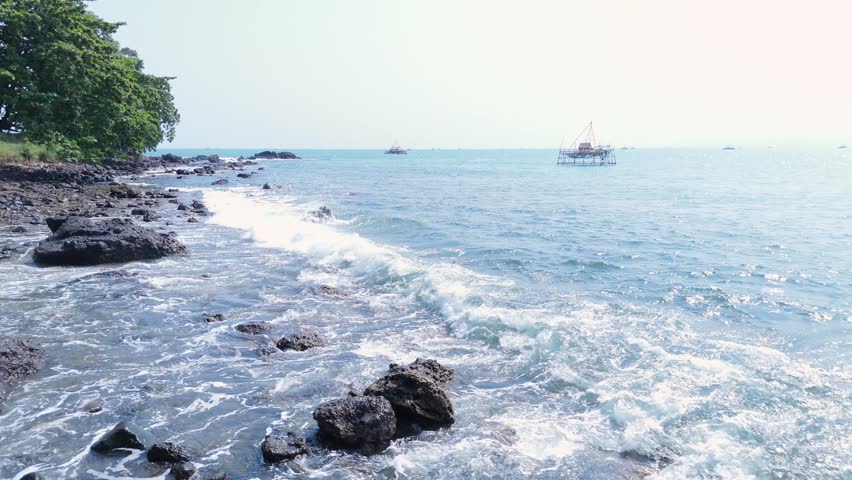 Scenic beach landscape with rugged rocks and crashing ocean waves under a clear blue sky