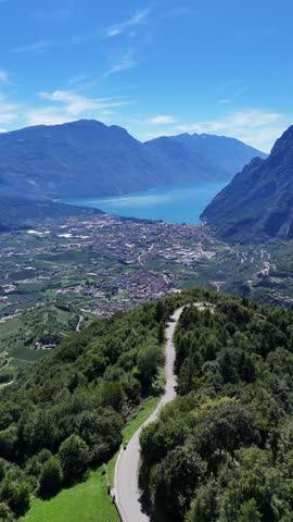 An Aerial view of a winding road descending toward Riva del Garda with Lake Garda and mountains beyond