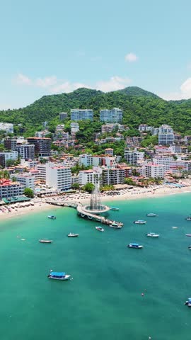Aerial view of Los Muertos Beach Pier extending into the turquoise waters of the bay, with boats anchored nearby and the hillside city of Puerto Vallarta, Jalisco, Mexico.