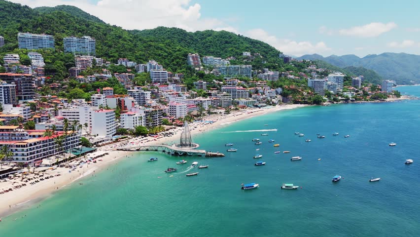 Aerial view of Los Muertos Beach Pier with boats anchored in the turquoise water along the coastline of Puerto Vallarta, Jalisco, Mexico.