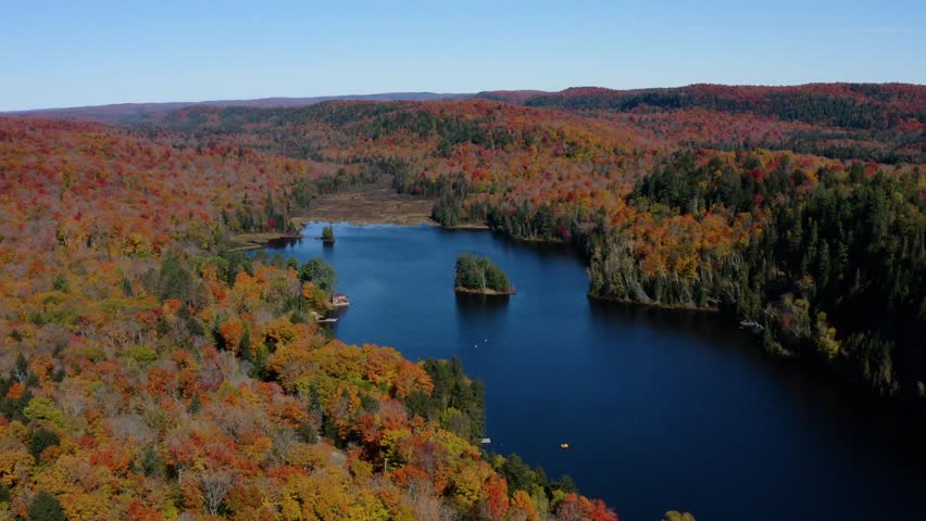 Cinematic drone view of a peaceful lake with small forested islands surrounded by vibrant autumn foliage in Ontario, Canada.