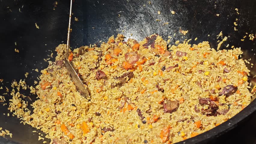 Cooking pilaf in a large pot with meat and rice in a busy kitchen
