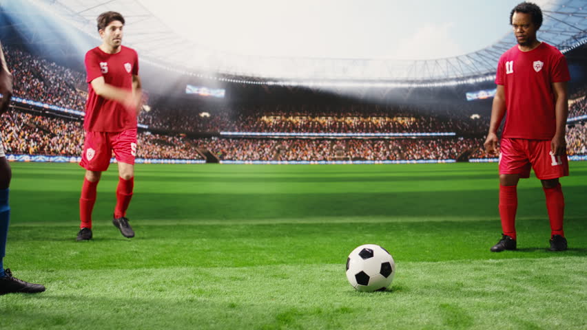 Lower body soccer players in red and blue uniforms dribbling each other for ball possession, running across pitch during match play, with footballers in motion blur.