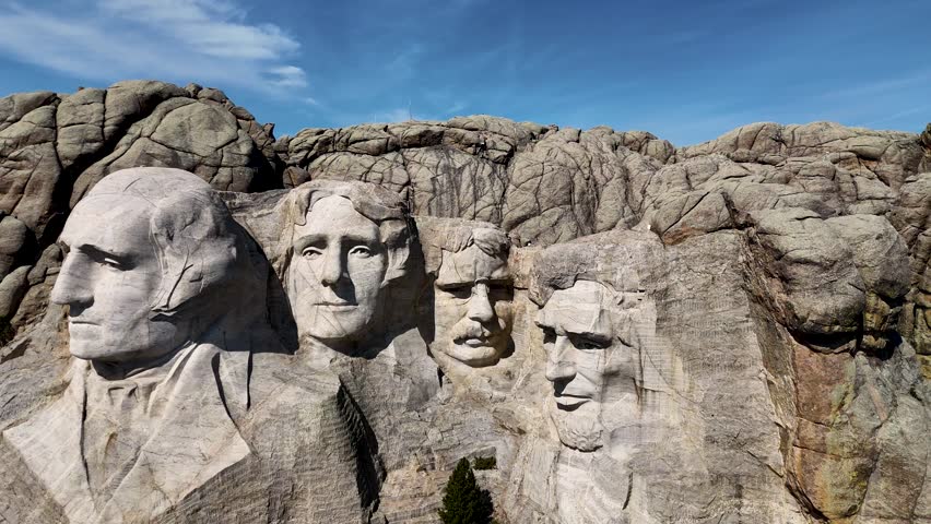 Cinematic drone footage of Mount Rushmore National Memorial in South Dakota, USA, showcasing the monumental granite sculptures of four American presidents surrounded by the scenic Black Hills