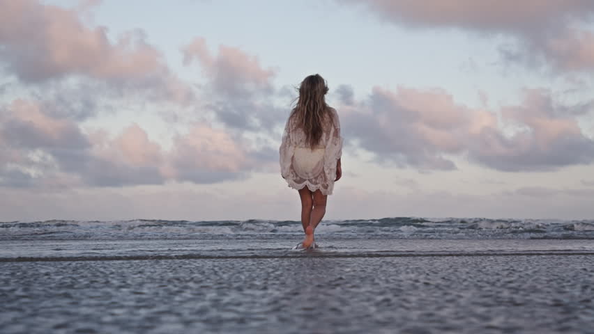 Joyful young girl strolls barefoot on Galveston Beach at sunset, soft waves and pastel sky creating a serene, dreamy coastal atmosphere.