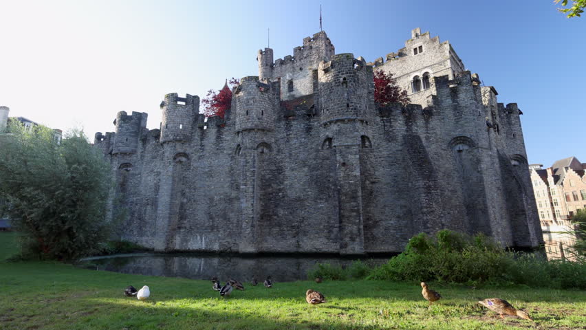 Gravensteen, a medieval castle in the city of Ghent in Belgium, Europe. Majestic Medieval Castle with Ducks on Green Lawn and Clear Blue Sky on a Sunny Day in Europe