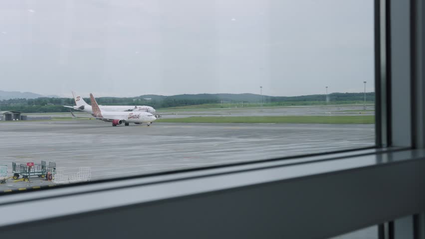 Kuala Lumpur, Malaysia - Agustus 10 2025 : Commercial airplanes parked on the airport apron and tarmac, viewed from inside the airport terminal through a glass window on an overcast day