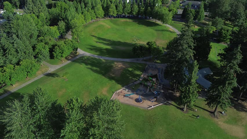 Recreation areas at Lake Meridian Park circular walking paths, green lawns, playground facilities by Seattle suburbs. Top-down view amenities encircled by tall evergreen trees in Kent, Washington. USA