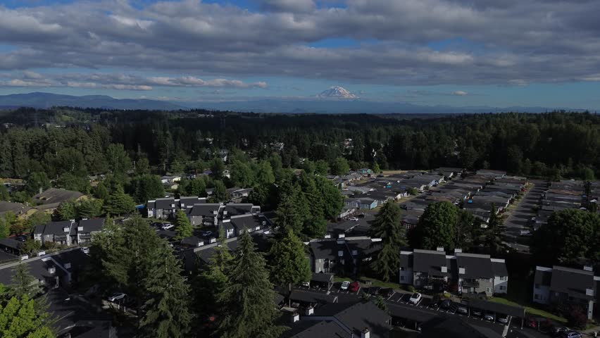 East Hill neighborhood display shows dense housing arrangements beside evergreen timberlines. Elevated drone perspective highlights residential roofs framed by Mount Rainier in Kent, Washington. USA