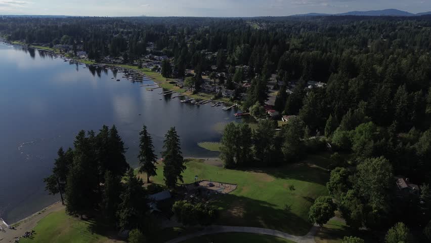 Lake Meridian Park shoreline features green park lawns bordering calm freshwater entry. Broad aerial viewpoint captures sprawling tree cover along residential waterfront in Kent, Washington. USA