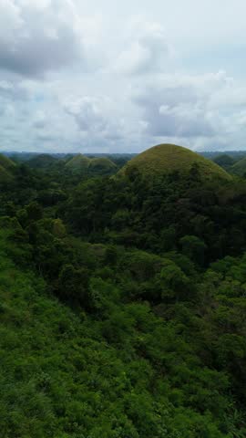 Aerial view of the iconic Chocolate Hills, a geological formation of grass-covered limestone mounds under a cloudy sky in Carmen, Central Visayas, Philippines.