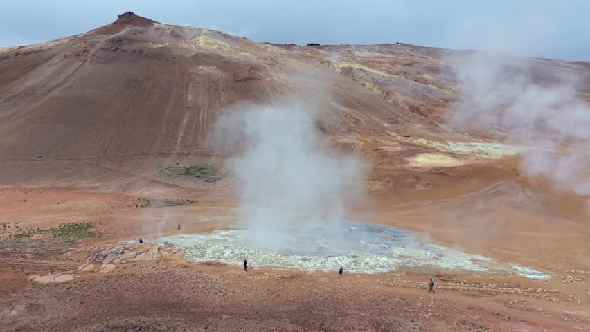 Tourists walking around a powerful fumarole emitting hot steam and gas in the volcanic landscape of Hverir, Namaskard geothermal area