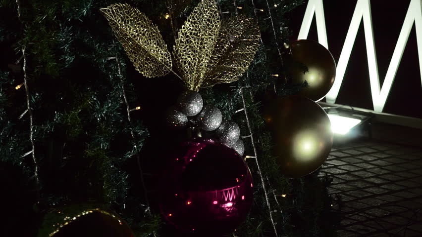 Close-up of Christmas tree ornaments with red and gold baubles, glitter leaves and warm lights, creating an elegant holiday decoration scene.