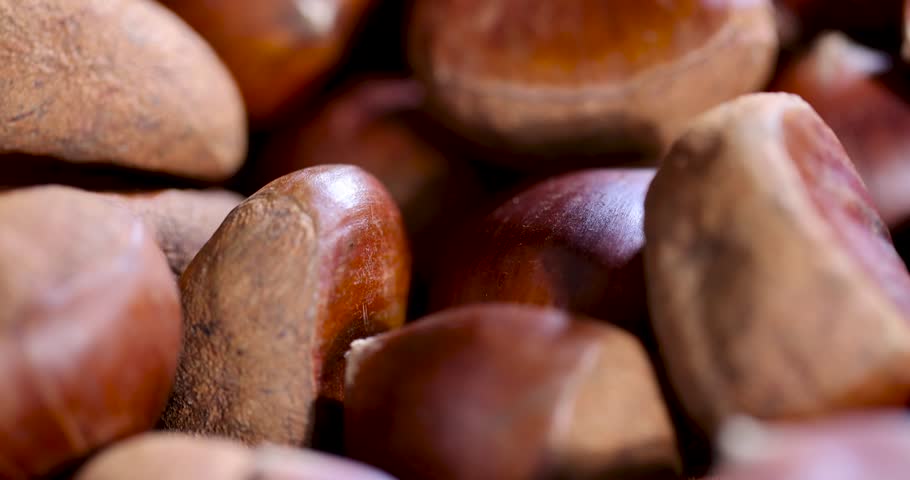 Smooth brown chestnuts, the chestnut fruit harvest is collected in a small bowl standing on a dark wooden surface with cracks.
