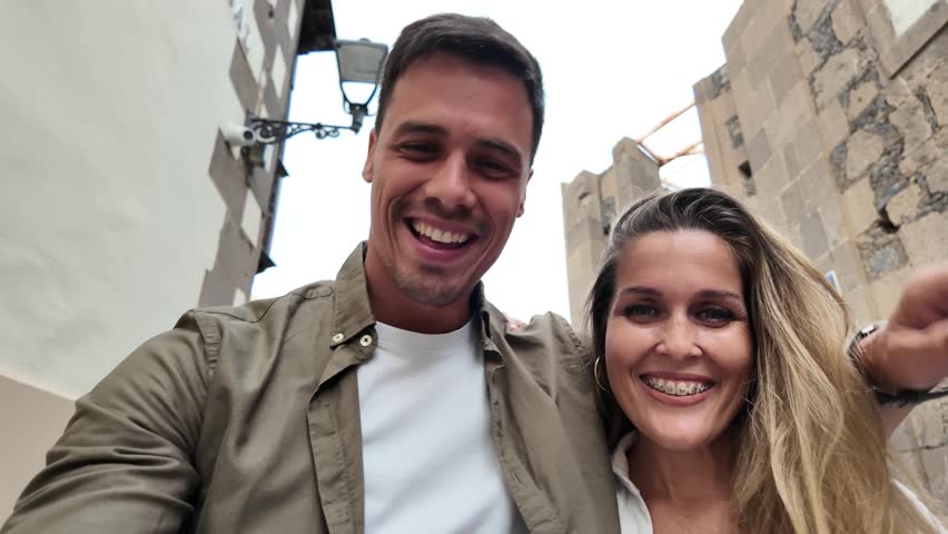Tourist couple enjoying a video call on a smartphone while walking through a charming historic town during their vacation.