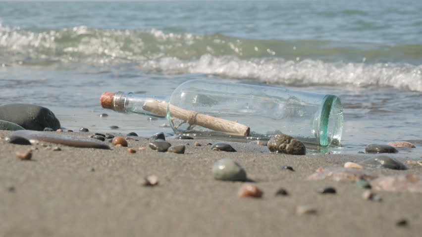 Glass bottle with paper note message inside on beach of sea.
