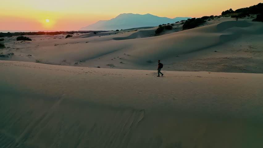 Patara sand dunes sunset aerial view with a man walking across the desert-like landscape in Kas, Antalya, Turkey. Majestic drone shot capturing solo traveler during golden hour.