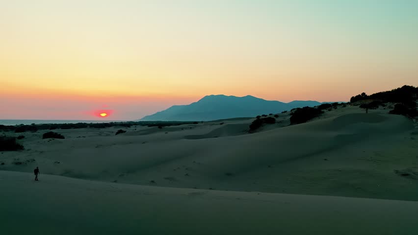 Patara sand dunes sunset aerial view with a man walking across the desert-like landscape in Kas, Antalya, Turkey. Majestic drone shot capturing solo traveler during golden hour.