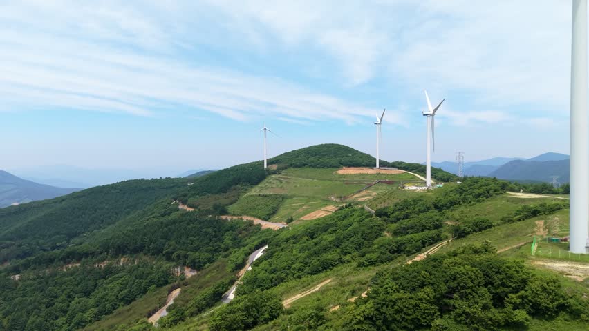 Forward flight approaches wind turbines atop Yukbaekmajigi ridge with clear blue sky over Pyeongchang mountains in South Korea