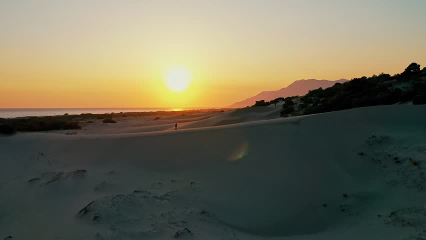 Patara sand dunes sunset aerial view with a man walking across the desert-like landscape in Kas, Antalya, Turkey. Majestic drone shot capturing solo traveler during golden hour.
