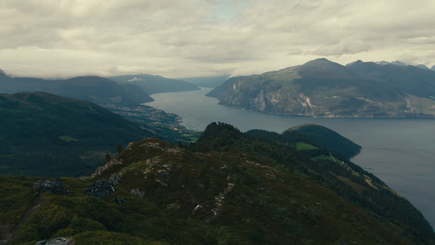 Long fjord cuts between forested ridges and rugged mountains at a Norwegian fjord, seen from a high aerial viewpoint.