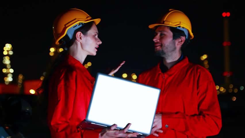 Teams engineers gas separation plants petrochemical plants stand together meetings during night shift holding tablets check data plan engineering work amidst the brightly lit modern energy industrial structure that operates 24 hours day.
