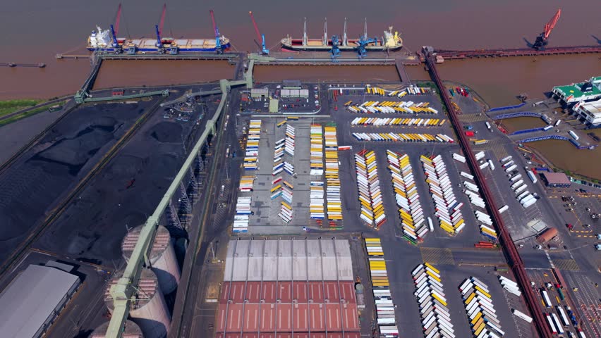 Aerial view of Immingham Bulk Terminal with cargo ships, cranes, and rows of trucks at the industrial port facility in South Killingholme, England, United Kingdom.