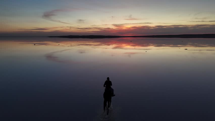 Aerial view of a person riding a horse on the reflective surface of Lake Tuz at sunset in Kulu, Konya, Turkiye.