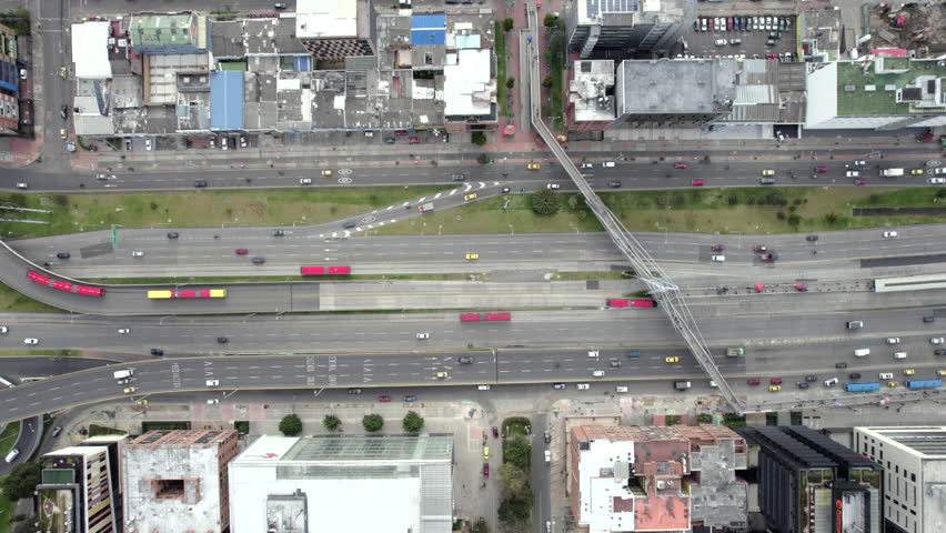 Drone follows a busy Bogotá highway with traffic, pedestrian bridge and surrounding buildings.