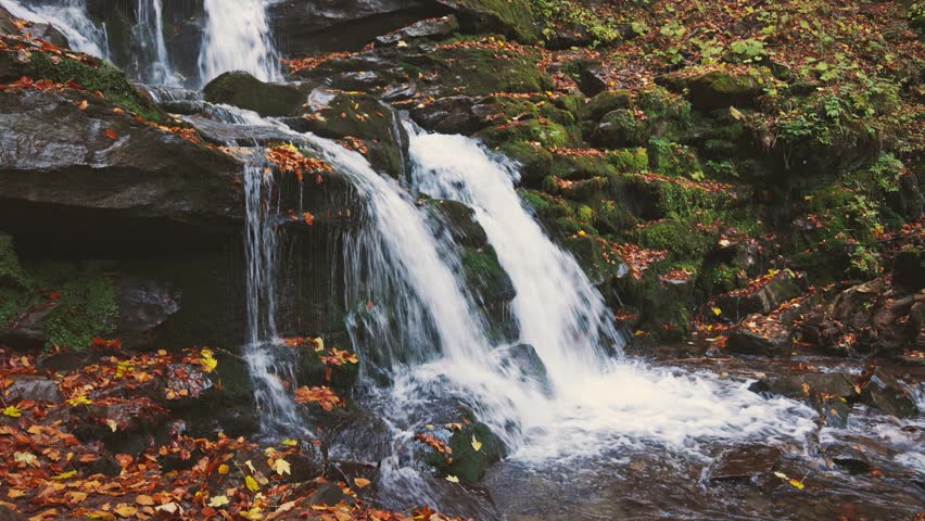 Waterfall falling down mountain slope in autumn forest