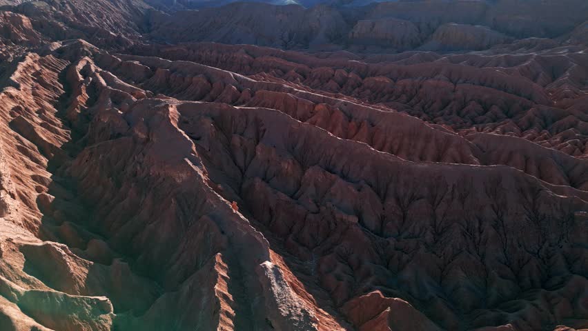 Aerial view of dramatic arid landscape featuring deep canyons and eroded rock formations of Atacama desert in Chile. Cinematic footage capturing vast mountain range in golden sunset light.