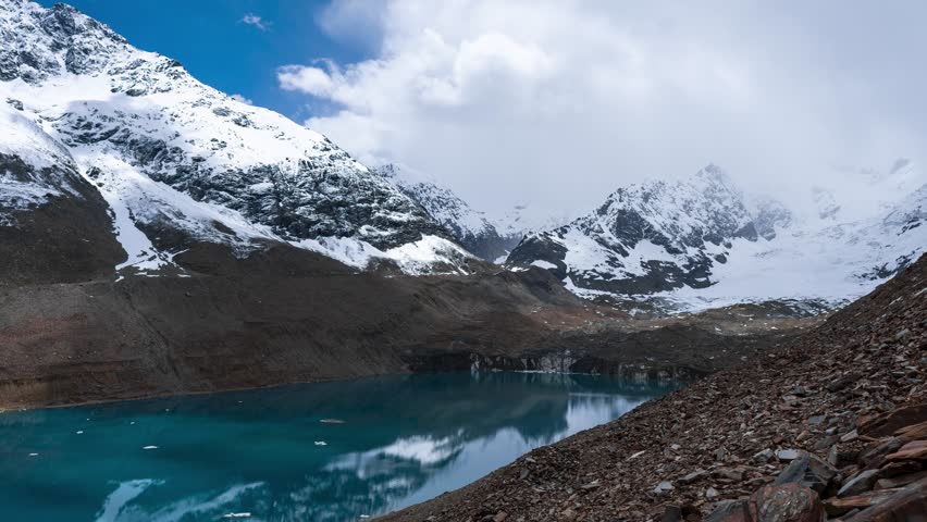 4K Timelapse of Ghepan Lake, snow covered mountains and clouds moving in sky at Lahaul, Himachal Pradesh, India. Natural landscape of India. Travel concept.  High altitude glacial lake in Himalayas.