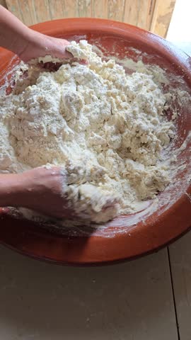 Hands kneading traditional Moroccan bread dough in a large clay bowl. Authentic homemade baking process showing flour being mixed and kneaded to prepare fresh artisan bread in a rustic kitchen.