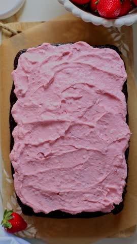 Spreading strawberry cream cheese frosting on chocolate sheet cake. Top view.