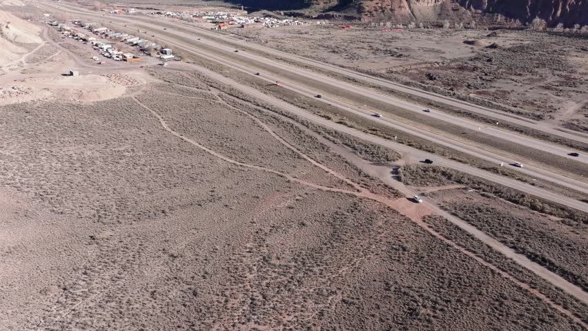 Aerial view of Interstate 70 cutting through the arid landscape with a mobile home park, sparse vegetation, and vehicles driving along the highway in Dotsero, Colorado, United States.