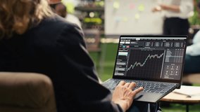 Businesswoman uses trading chart with financial data on laptop screen, typing market indicators for analytics, employee working in modern informal outdoor space. - Powered by Shutterstock - Get 15% off with code: PIKWIZARD15