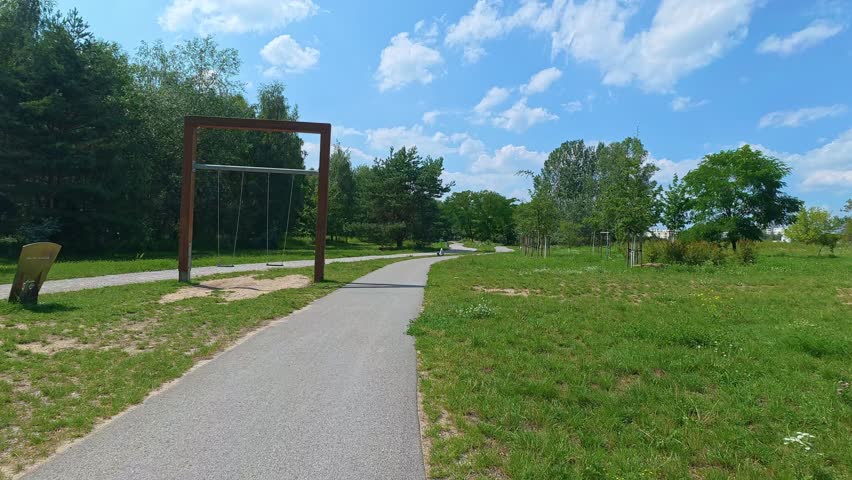 Paved path winding through green park with wooden swing structure.