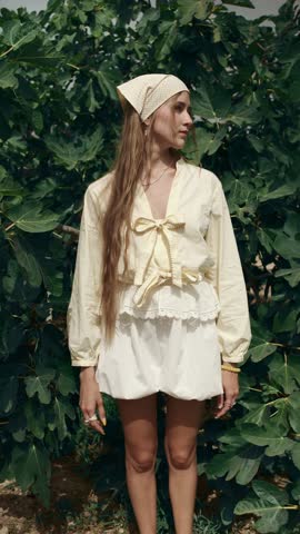 Stunning young woman in vintage style clothing posing in front of a fig tree. Long haired model with a bandana in a sunny garden