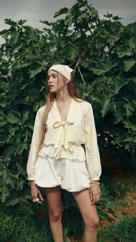 Stylish beautiful woman with long blonde hair posing in front of a fig tree. Young female model enjoying a sunny day in the countryside