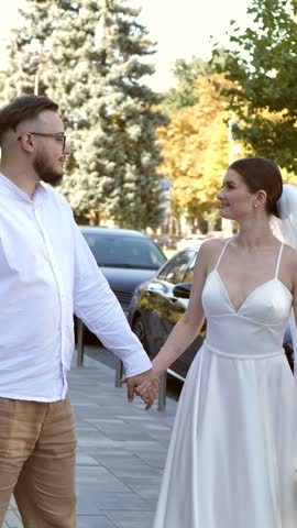 Happy newlywed couple kissing on city street while bride holding wedding bouquet.