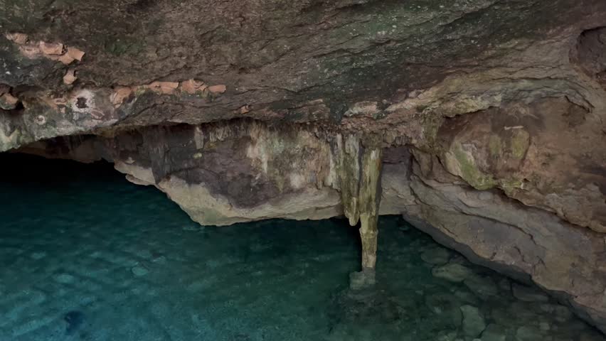 Vertical panning shot of a crystal-clear underground cave pool and stalactites in a natural cenote.