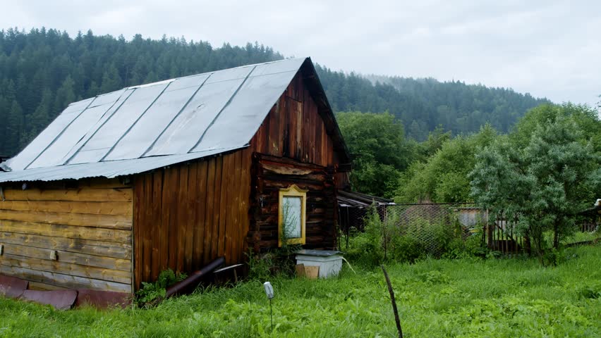 Wooden cabin in forest village surrounded by green trees and misty mountains. Rustic house creates peaceful rural atmosphere close to nature