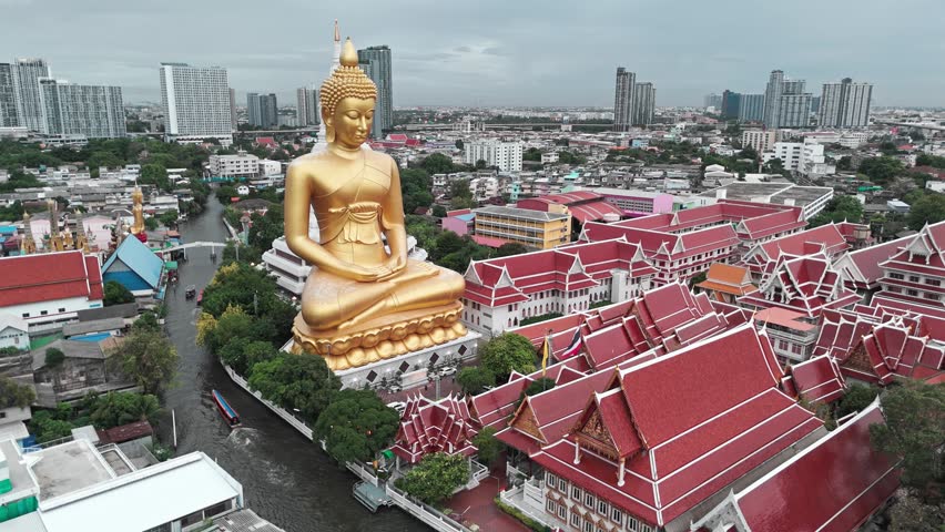An aerial view of the giant golden Buddha statue at Wat Paknam Phasi Charoen in Bangkok, surrounded by temple roofs and canals