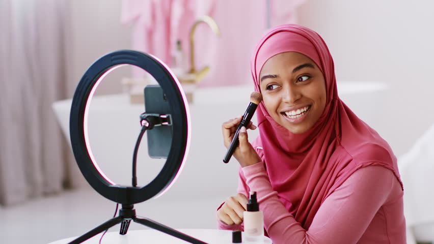 Smiling Young Muslim Woman Applying Makeup In Front Of Ring Light, Home Setting, Beauty Concept