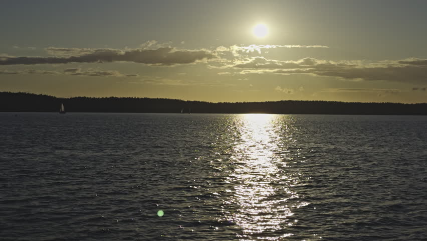 A Golden sun reflecting across rippling lake water, with distant shoreline silhouetted at dusk