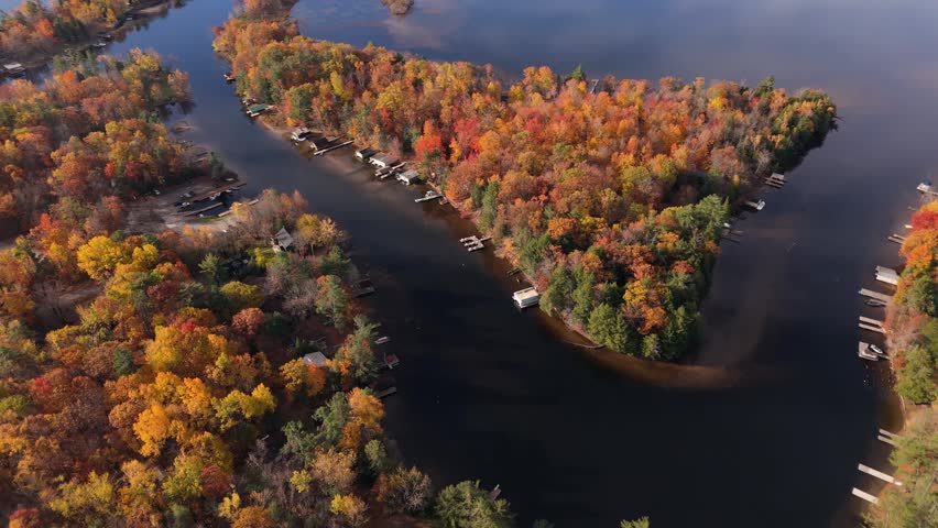 An overhead view of a narrow river channel cutting through vibrant autumn forest and lakeside homes