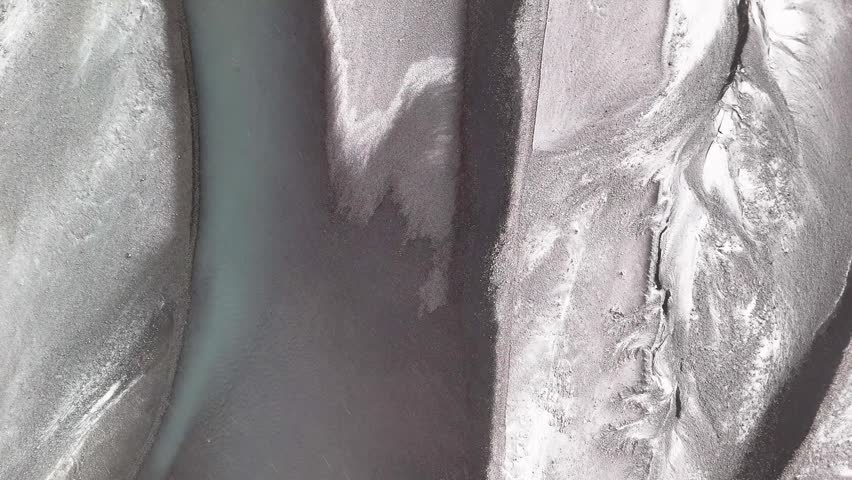 A drone view of frozen river channels stretching across icy terrain during winter sunrise in Lomagnupur, Iceland